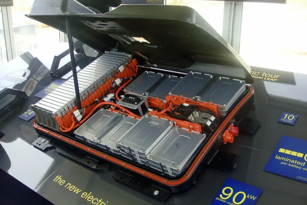 Vista superior de un pack de baterías de coche eléctrico con módulos metálicos conectados por cables de alta tensión naranjas