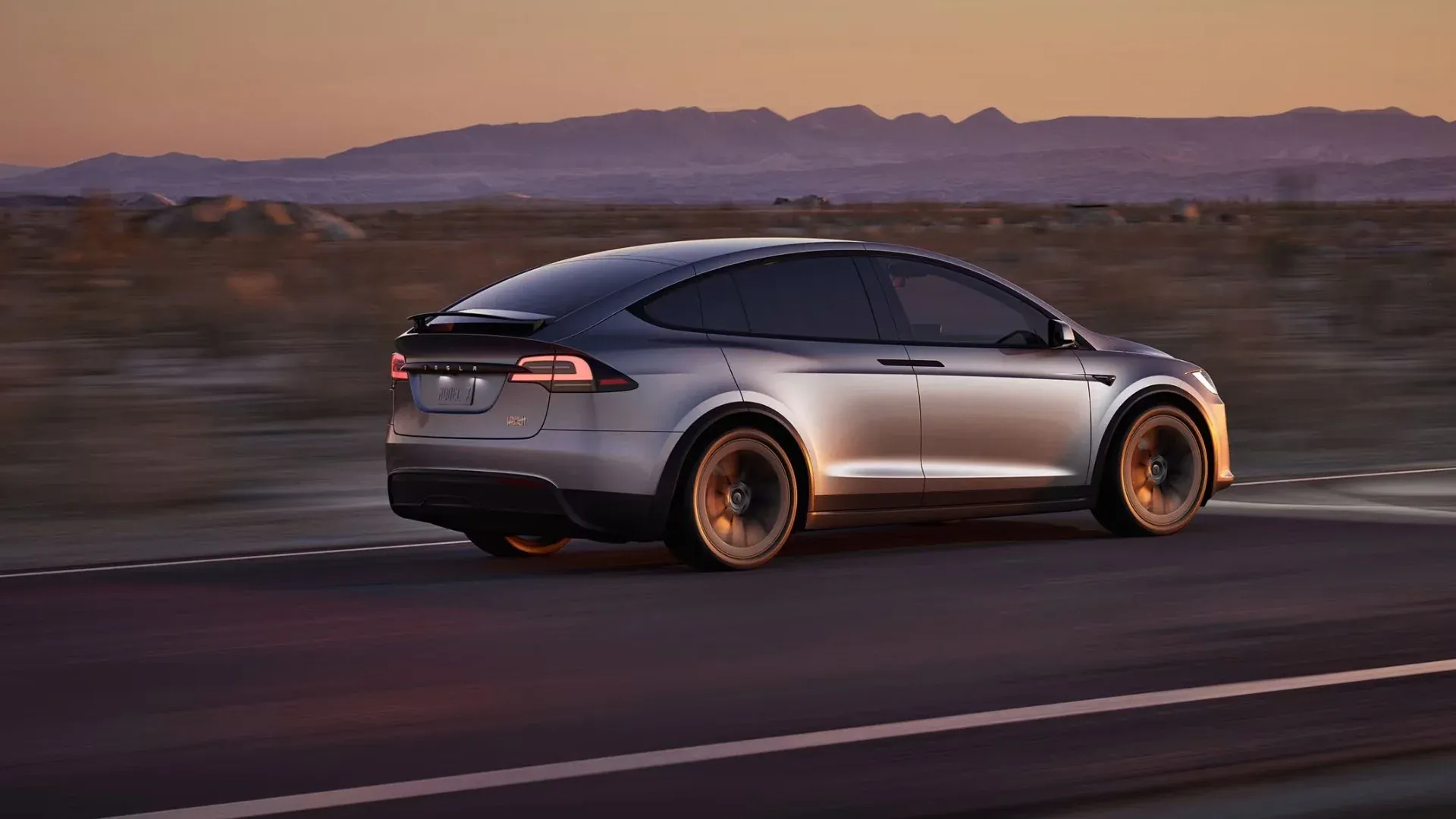 Un Tesla Model X plateado en un camino desértico con un hermoso atardecer de fondo.