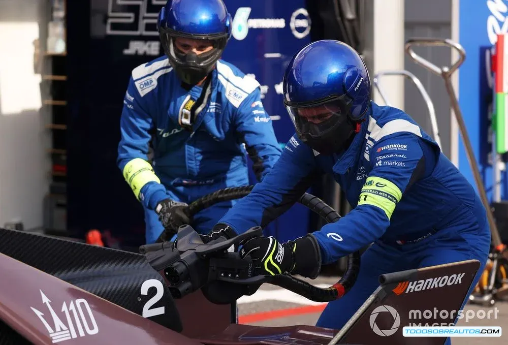 Un equipo de mecánicos trabajando en un coche de Fórmula E durante una parada en boxes, enfocándose en la carga de la batería.