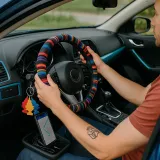 Mano tatuada ajusta volante multicolor; interior azul eléctrico, ambientadores colgantes y GPS activo revelan estilo y tecnología personal.