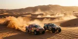 Un Ford Raptor T1+ y un Dacia Sandrider compitiendo lado a lado a alta velocidad, levantando grandes estelas de polvo