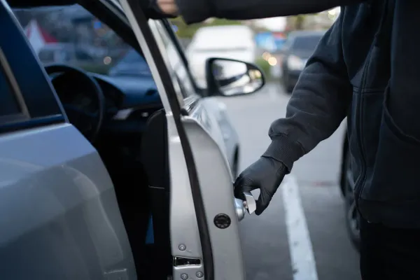 Persona con abrigo y guantes negros abriendo puerta de auto plateado