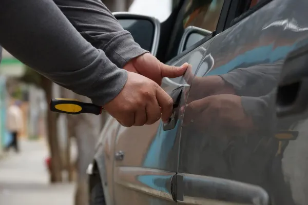 Manos con destornillador forzando cerradura de auto gris