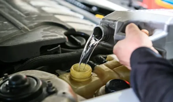 Mano vertiendo augua con un envanse en almacenador de agua de auto