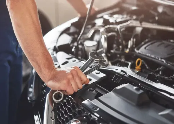 Mano sosteniendo llaves dos llaves y de fondo la parte delantera de una auto con el capo abierto